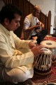 Udit Pankhania tunes his Tabla. The skin is tensioned by a number of cords that run down the sides; inside each pair of cords is a large wooden toggle. The further down the barrel of the drum the toggle is moved, the tighter the skin is made, raising the pitch.\n\nThe black circles in the middle of each drum skin, which enable an even wider variety of sounds to be made, are built up in layers of rice starch mixed with coal dust.